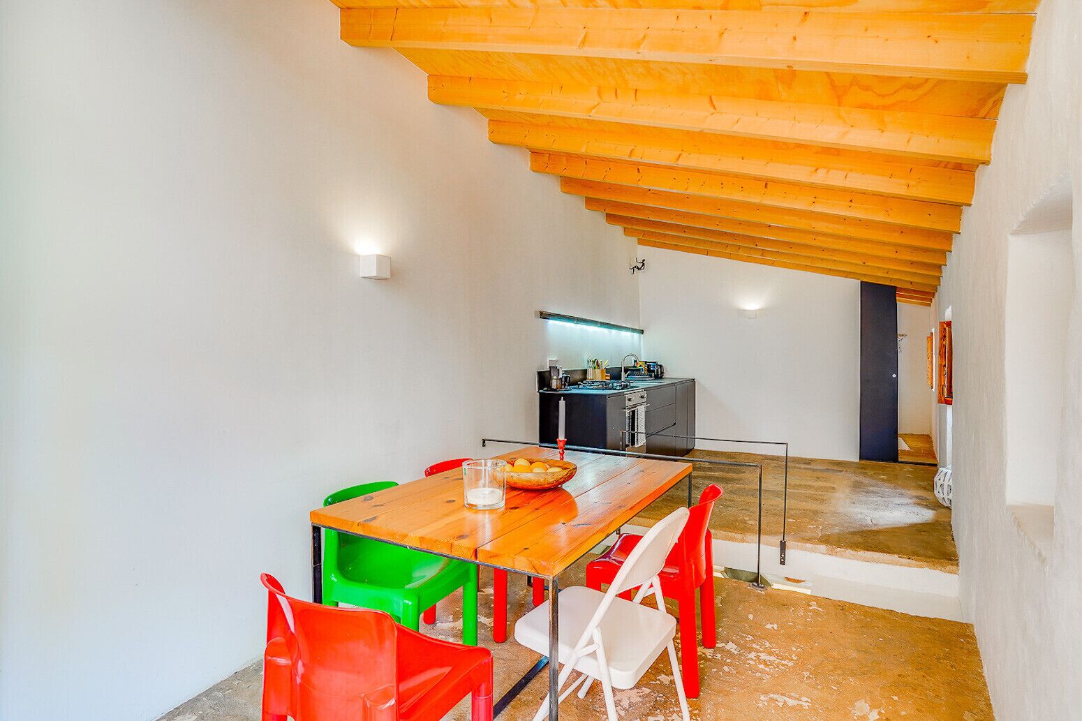 A compact kitchen with modern appliances, a dining area with mismatched chairs, and a wooden ceiling.