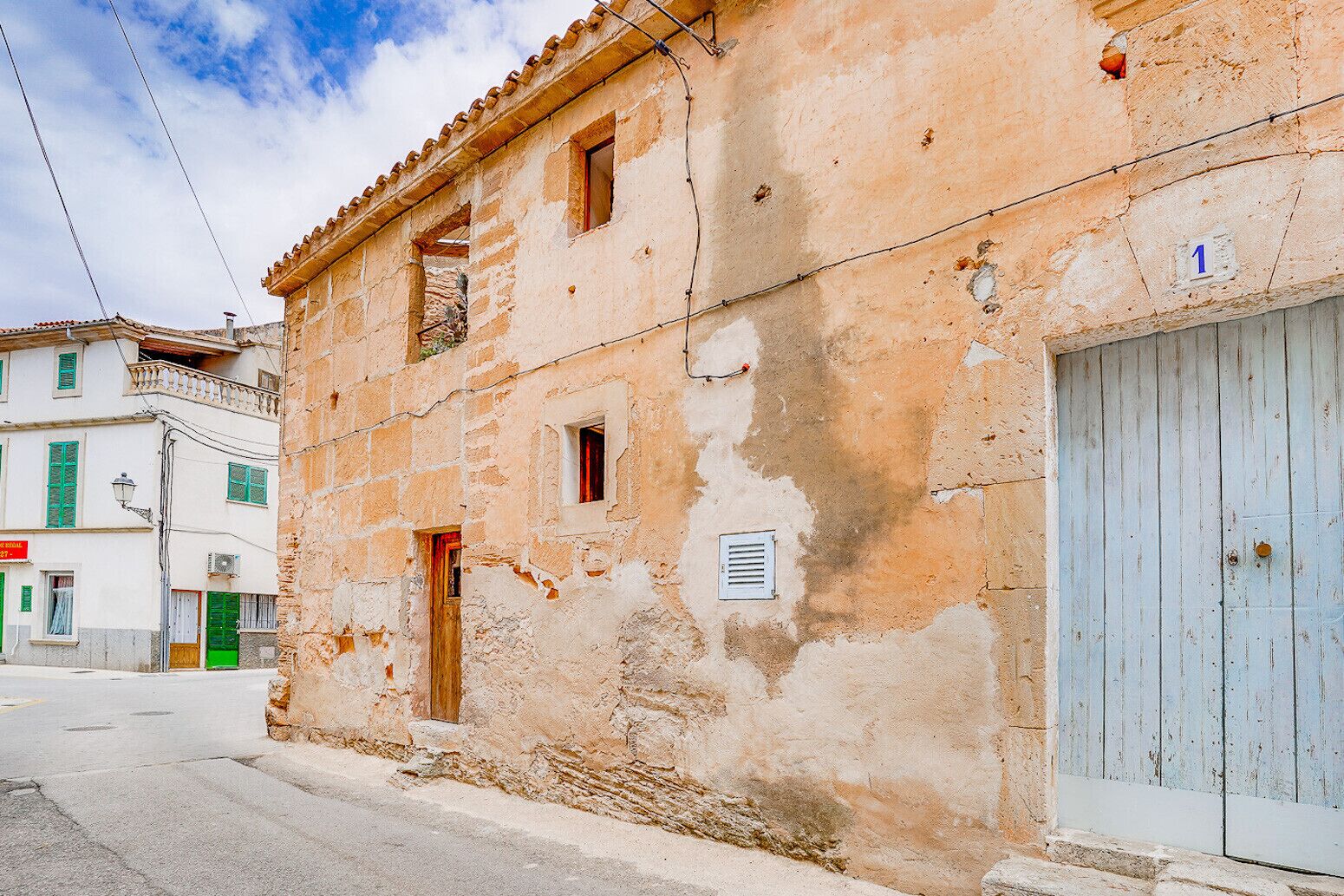 Un edificio desgastado con una sola puerta visible y un ventanal pequeño, al lado de una calle.