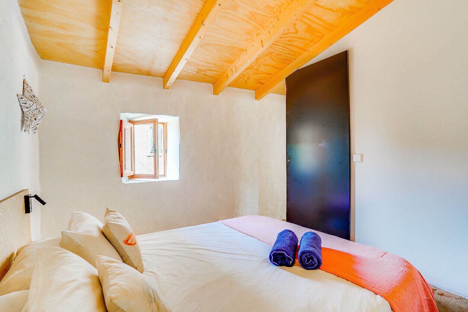 Een slaapkamer met een houten plafond, een bed met witte lakens, een raam met uitzicht en een deur.