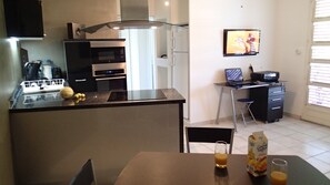 Une cuisine moderne avec un coin repas, un téléviseur fixé au mur et un petit espace bureau.