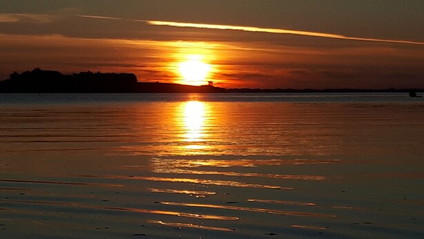 Una puesta de sol sobre una playa con aguas tranquilas que reflejan el sol.
