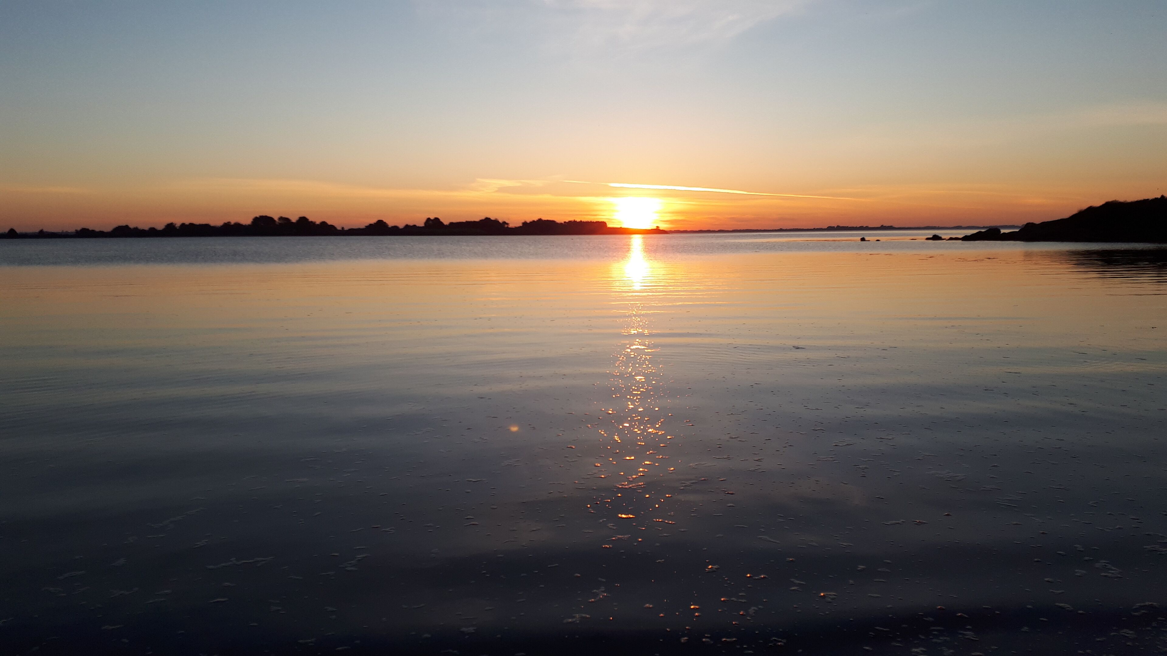 Un coucher de soleil sur une étendue d’eau calme, avec un horizon dégagé.