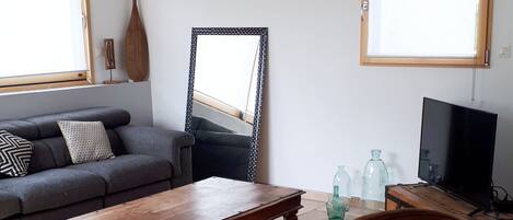 Ett vardagsrum med en soffa, ett soffbord, en fåtölj i läder, en tv och ett fönster med persienner.