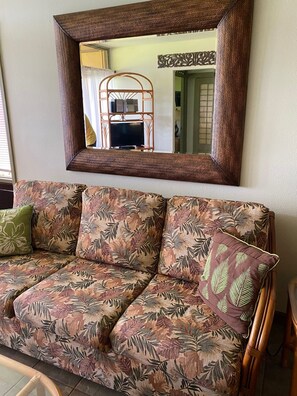 A sofa with a floral pattern, a mirror above it, and a wooden chair to the right.