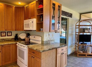 A kitchen with wooden cabinets, a microwave, a stove, and a wooden TV stand. - Beaches, Beaches, Beaches! West Molokai. Remote and Private. Hawaii's best. (Maunaloa)