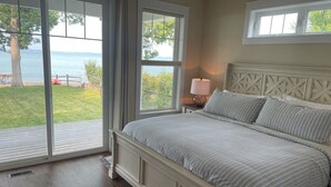 A bedroom with a large bed, a nightstand, a lamp, and a view of the outdoors.