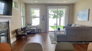 A living room with a fireplace, a sofa, a dining table, and a view of the outdoors.