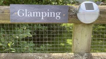 A sign reading "Glamping" attached to a wooden fence with a solar panel.