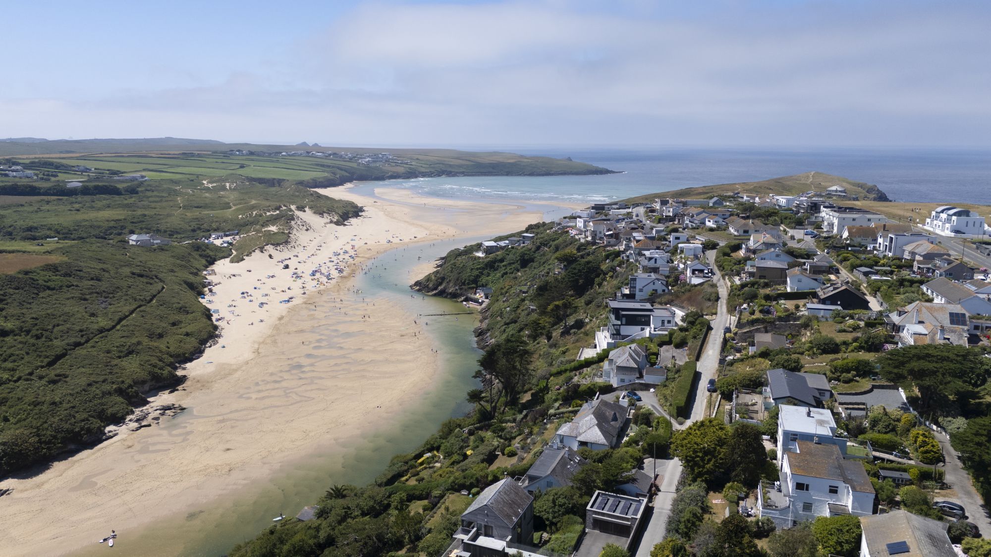 Vue aérienne d’une ville côtière avec une plage, des maisons et une petite colline surmontée d’un bâtiment.