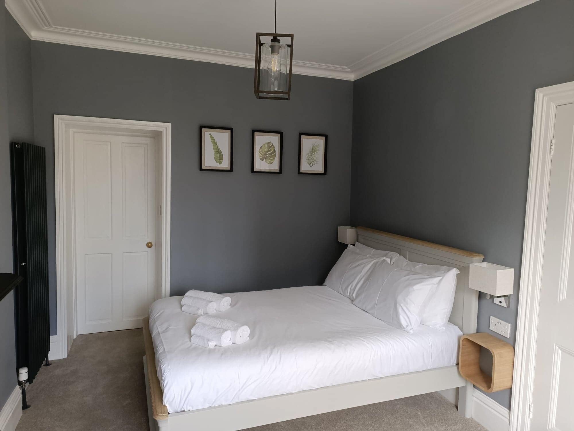 A bedroom with a bed, a white door, and framed botanical prints on the wall.