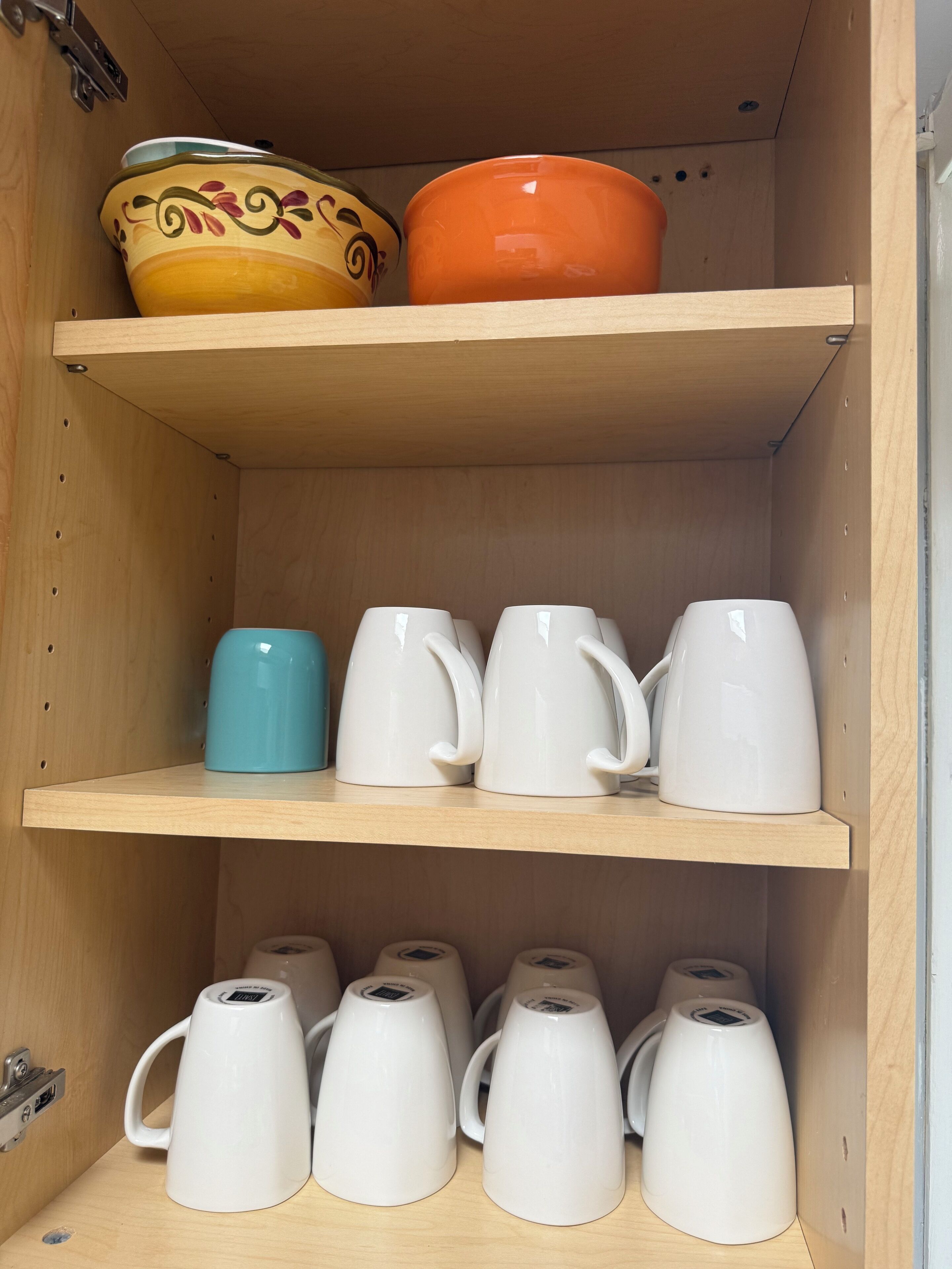 A wooden shelf unit with various ceramic mugs and a decorative bowl.