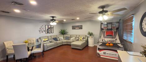 A modern living room with a sectional sofa, a glass coffee table, and a dining area with chairs.