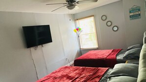 A bedroom with two beds, a ceiling fan, a TV mounted on the wall, and a window with blinds.