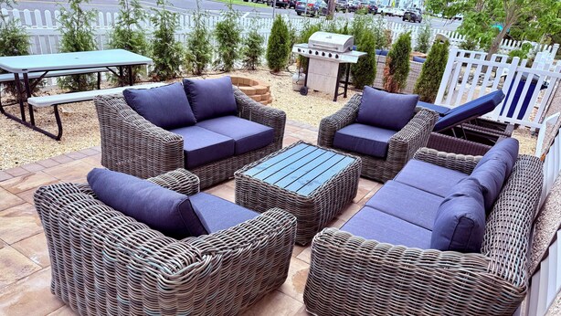 A patio area with wicker furniture, including sofas and a coffee table, and a barbecue grill.
