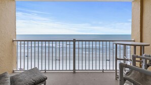 A balcony with a view of the beach, a small table, and a cushioned chair. - Direct Oceanfront View from Nearly Every Room! Great Getaway Near No-Drive Beach (New Smyrna Beach)