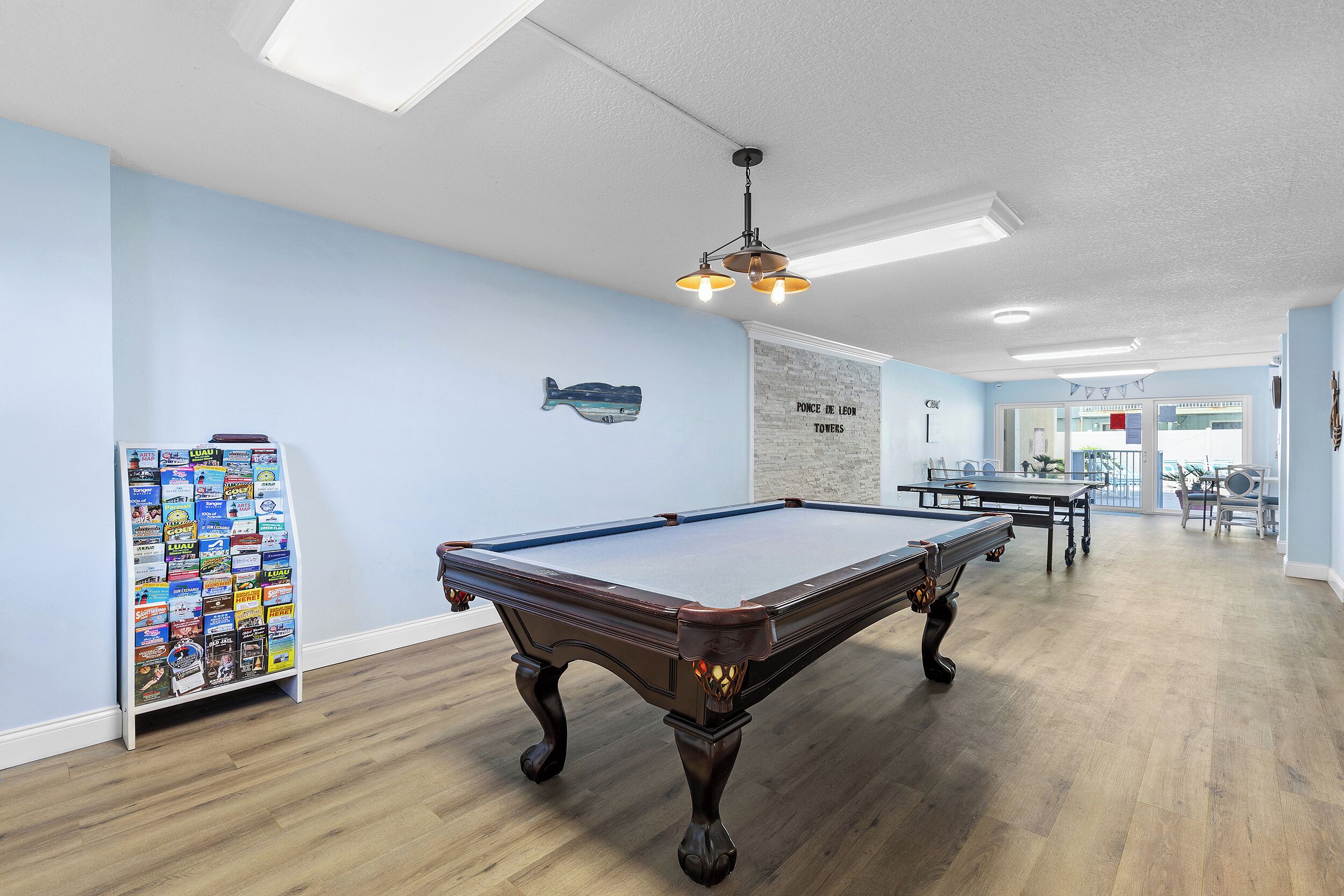 A pool table in a room with light blue walls, a wooden floor, and a ceiling light fixture.