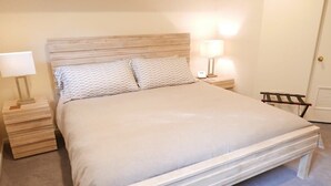 Een netjes opgemaakt bed met een houten hoofdeinde, twee bedlampen en een klein nachtkastje van hout.