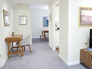 A hallway with a dining area, a TV, and a kitchen area.