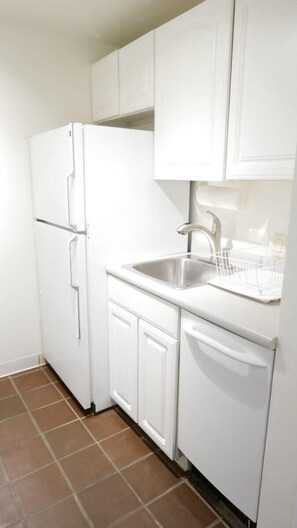 A compact kitchen with white cabinetry, a stainless steel sink, and a dish rack.