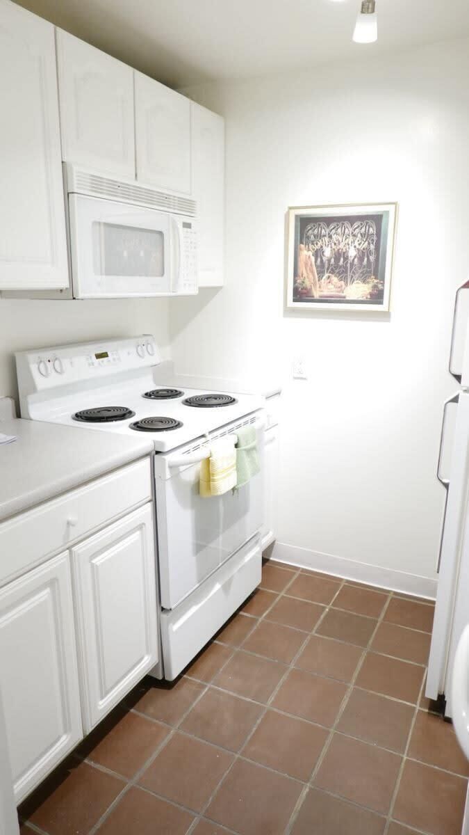 A kitchen with white cabinets, a white stove, and a microwave.