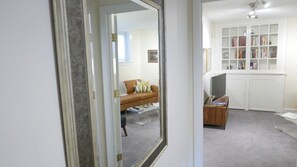 A room with a large mirror, a sofa with cushions, a wooden side table, and a bookshelf.
