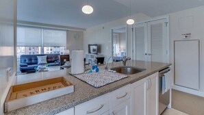Een moderne keuken met een granieten aanrecht, witte kasten, een spoelbak en een zithoek met een bank en salontafel.