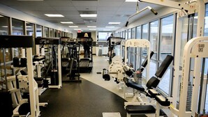 Een sportschool met diverse fitnessapparaten, een loopband en een machine voor het bankdrukken.