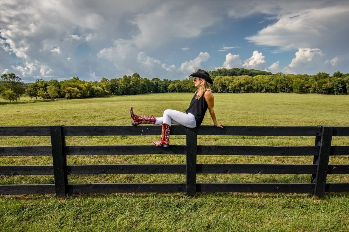 A person sitting on a wooden bench in a grassy field with trees in the background.
