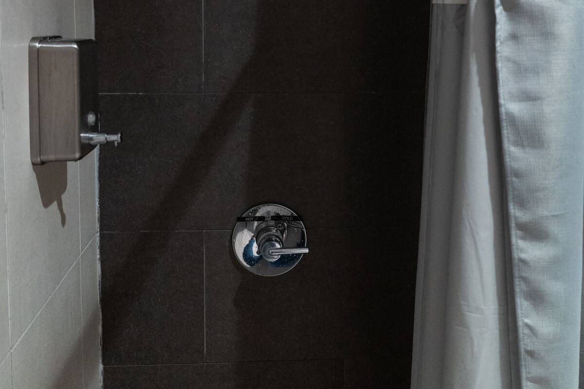 A shower area with a handheld showerhead, a wall-mounted control panel, and a curtain.