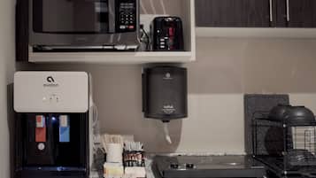 Una cocina equipada con microondas, tostadora, dispensador de agua, cafetera y escurreplatos.