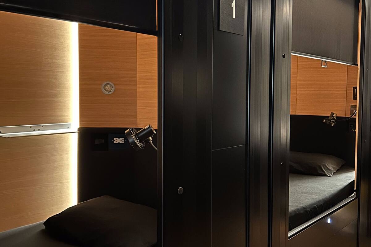 A compact, modern train compartment with bunk beds, a small table, and a red pipe overhead.