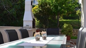 An outdoor dining area with a glass table, metal chairs, and a white barbecue grill in the background. - Apartment in Banjol with Balcony, Air condition, WIFI, Dishwasher (4888-1) (Banjol)