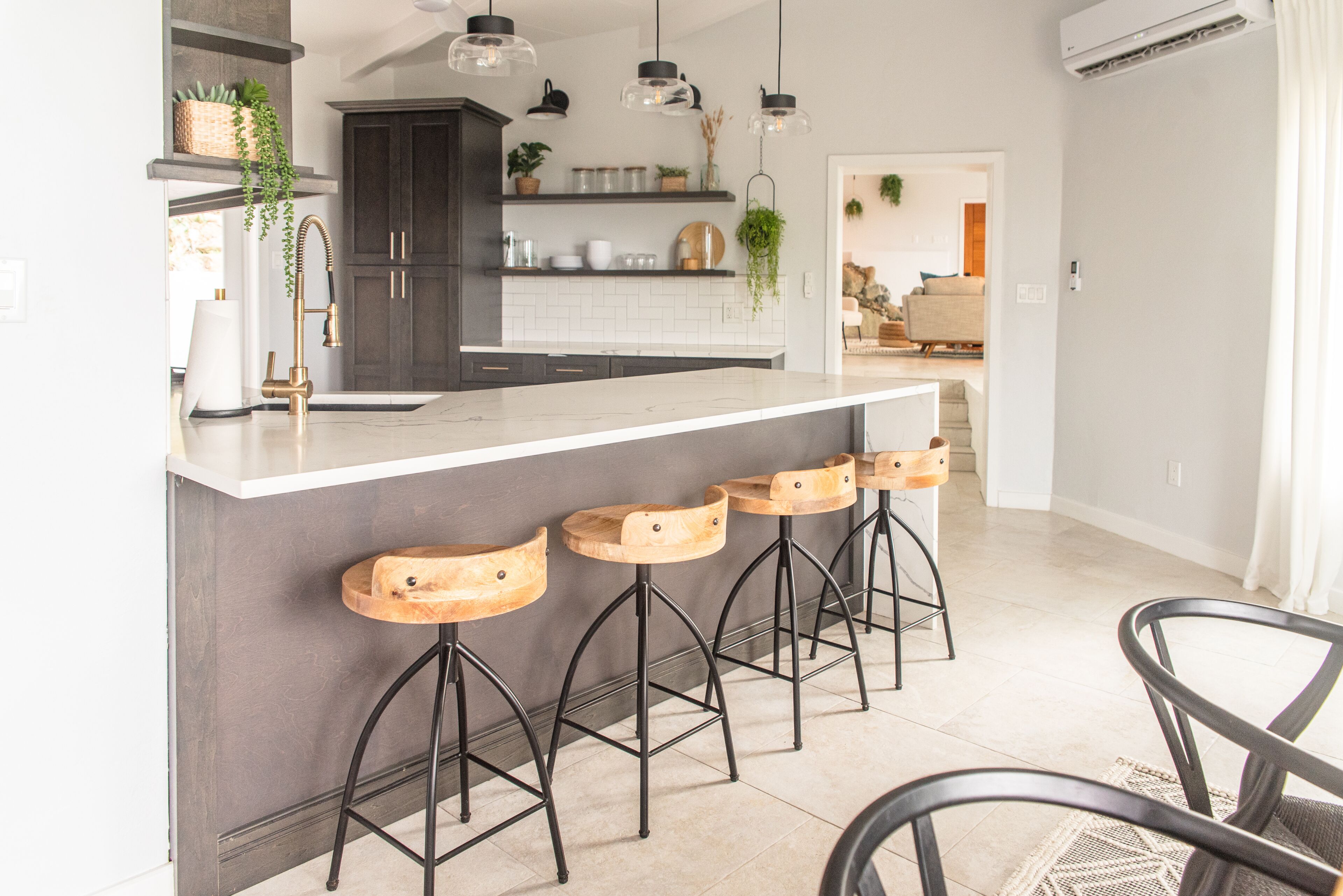 A modern kitchen with a white countertop, dark cabinets, and bar stools.