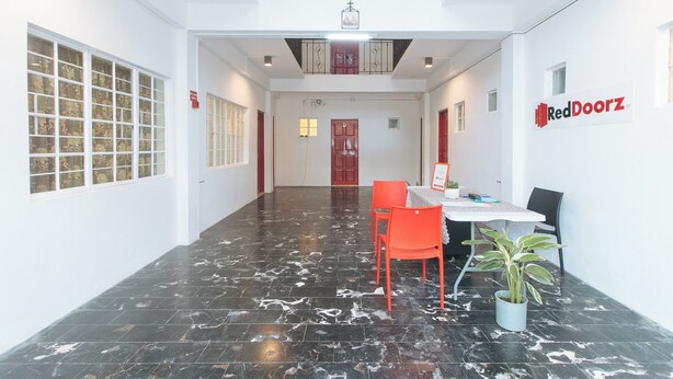 A hallway with a reception desk, red chairs, a potted plant, and a sign reading "RedDoorz". - Reddoorz @ V-cloud Hills Near De La Salle (Dasmarinas)