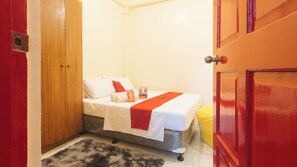 Una habitación pequeña y ordenada con una cama, un armario de madera y una puerta roja.