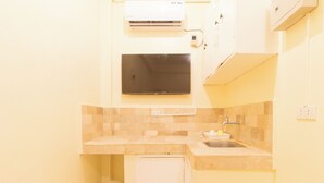 A compact kitchen with a built-in TV, a small sink, and an air conditioning unit. - Reddoorz @ V-cloud Hills Near De La Salle (Dasmarinas)