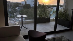 A modern living room with a sofa, a glass coffee table, and a view of the sunset through large windows. - Polo 54 Downtown Apartments (Playa del Carmen)