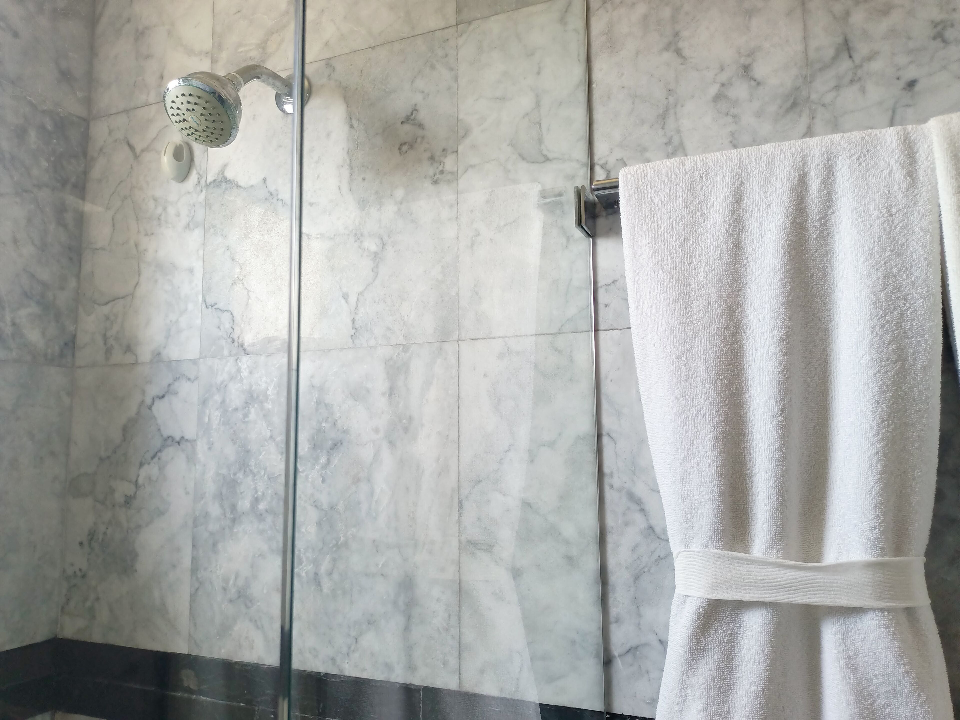 Une salle de bain aux murs recouverts de marbre, avec une douche en verre et une serviette blanche suspendue à un porte-serviettes.