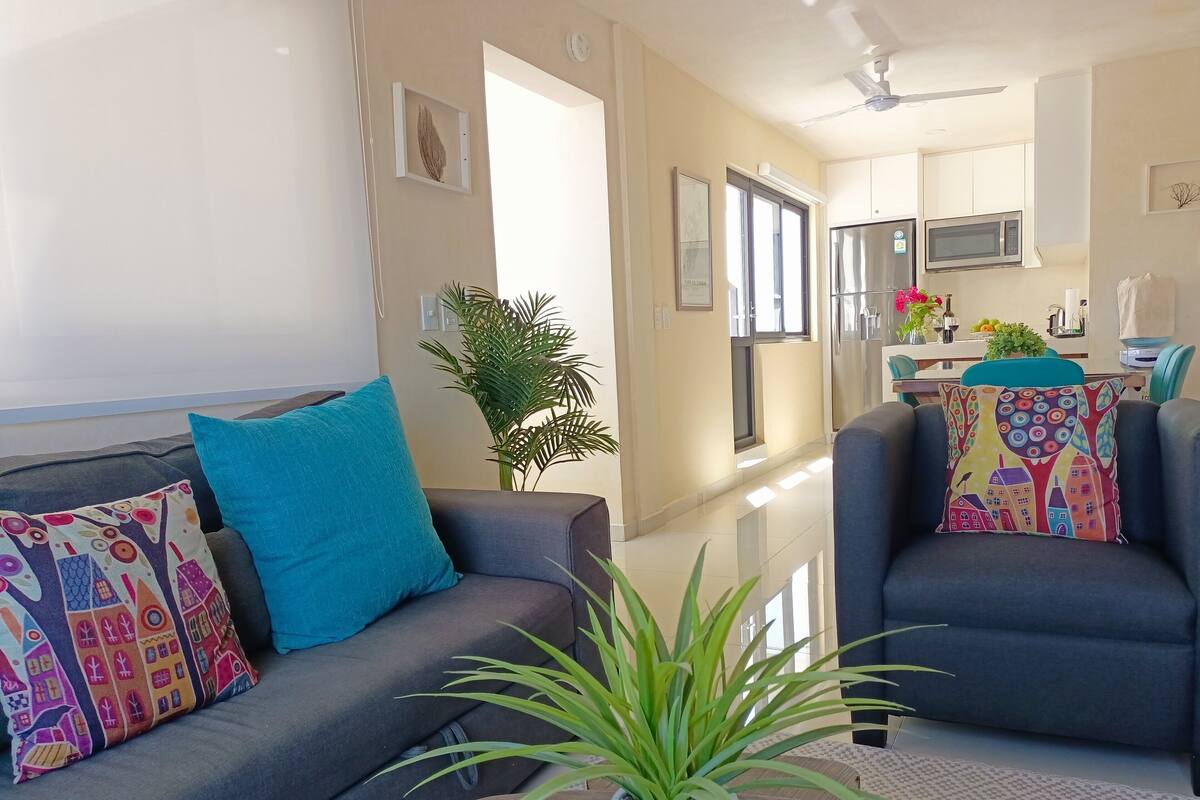 Ein modernes Wohnzimmer mit einem grauen Sofa, Türkis-Kissen und einer Topfpflanze.