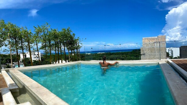 A rectangular infinity pool with clear blue water, surrounded by a wooden deck and a stone wall. - Polo 54 Downtown Apartments (Playa del Carmen)