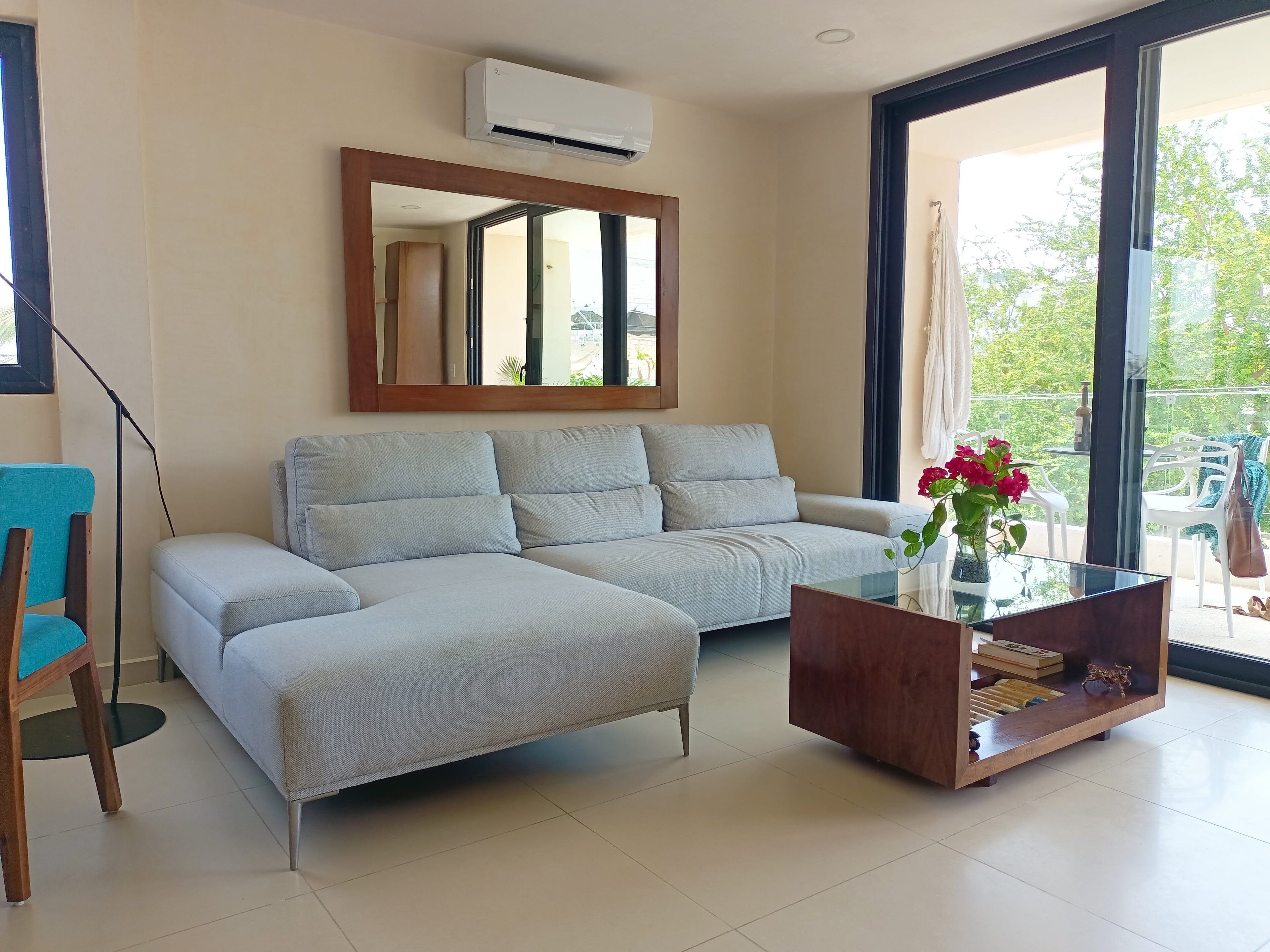 A modern living room with a sofa, a glass coffee table, and a large mirror.