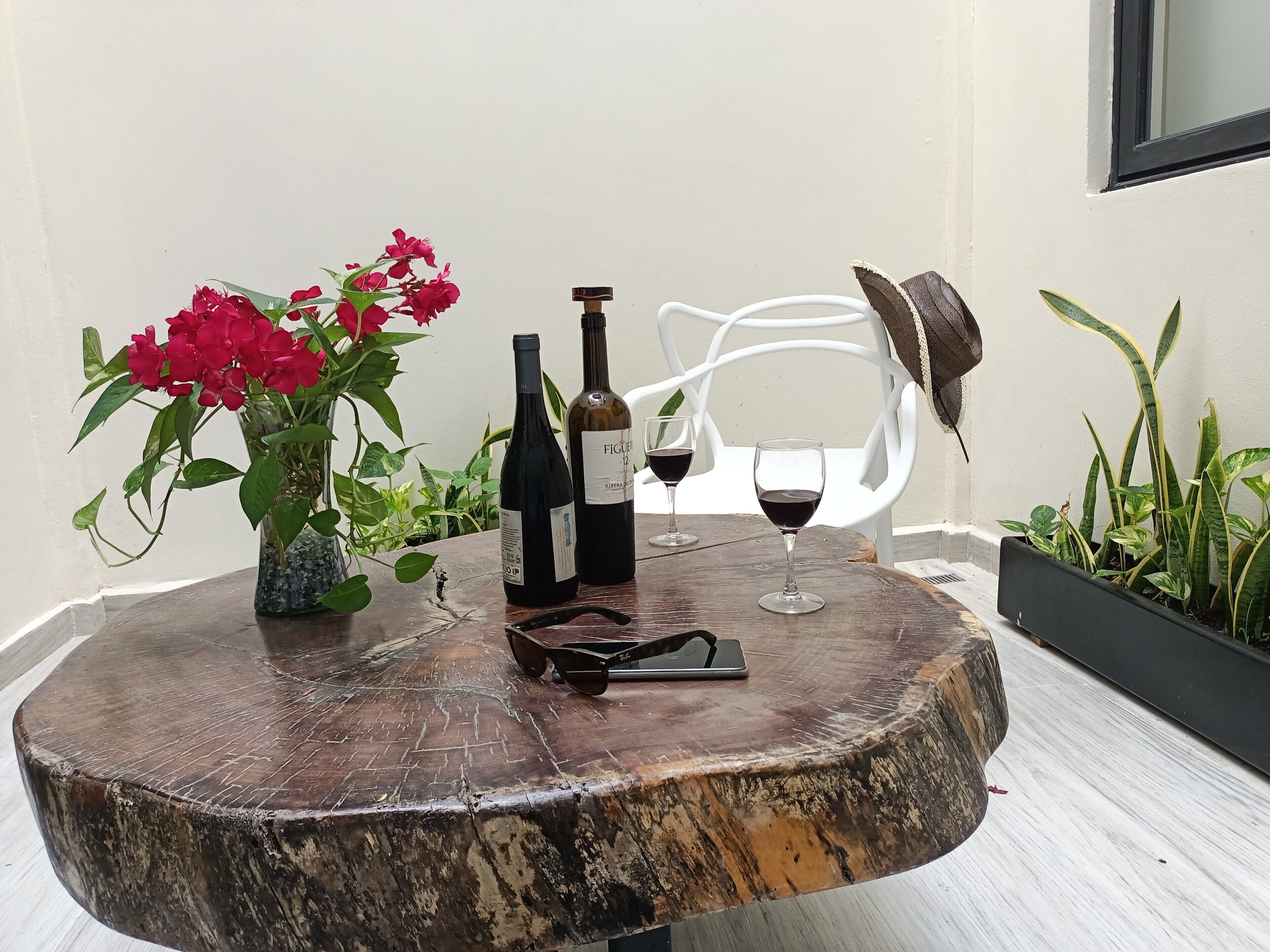 Ein runder Holztisch mit einer Vase voller roter Blumen, zwei Weinflaschen und zwei Weingläsern.