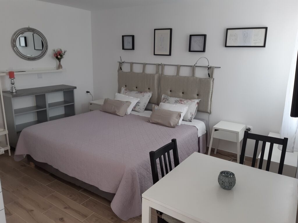 A bedroom with a large bed, a bedside table, a chair, a small table, and a mirror on the wall.