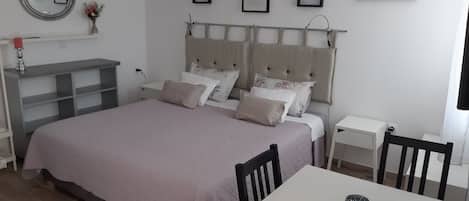 A bedroom with a large bed, a bedside table, a chair, a small table, and a mirror on the wall.