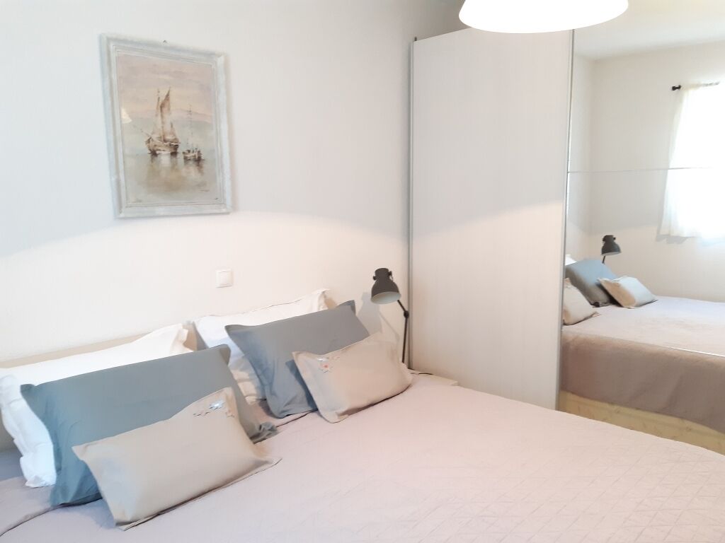 A bedroom with a bed, pillows, a bedside lamp, a mirror, and a framed picture on the wall.