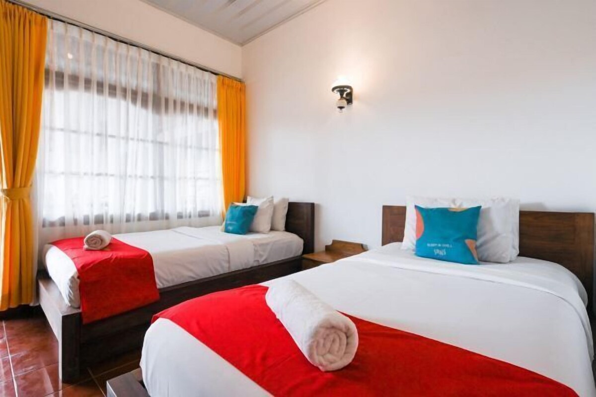 A hotel room with two beds, each with red and white bedding, and a window with yellow curtains.