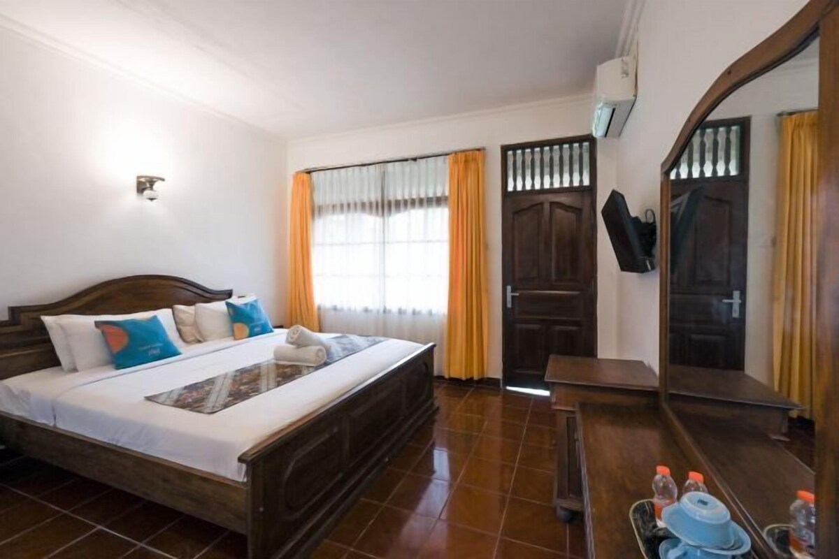 A hotel room with a wooden bed, a television mounted on the wall, a window with curtains, and a door.