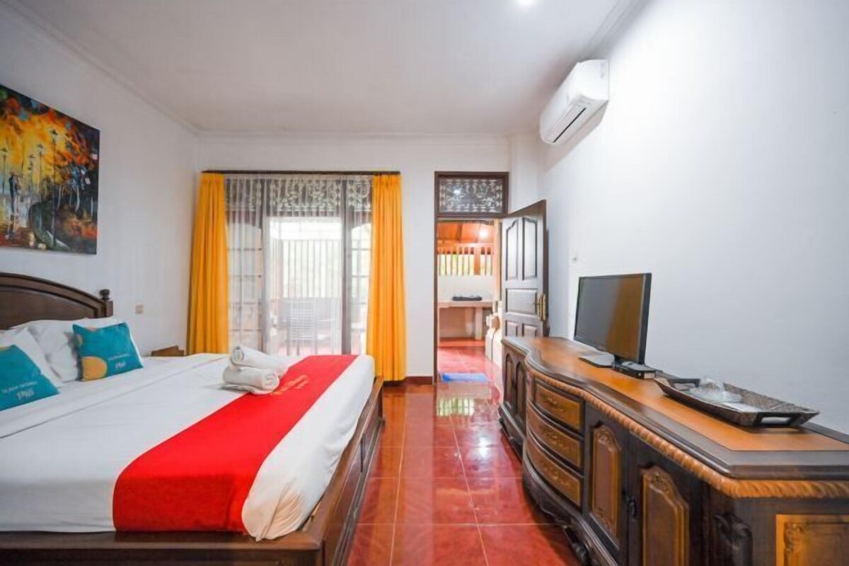 A hotel room with a bed, a TV, a wooden dresser, and a window with curtains.
