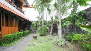 Une cour bordée d’un mur de pierre, d’une clôture en bois et agrémentée de diverses plantes tropicales.
