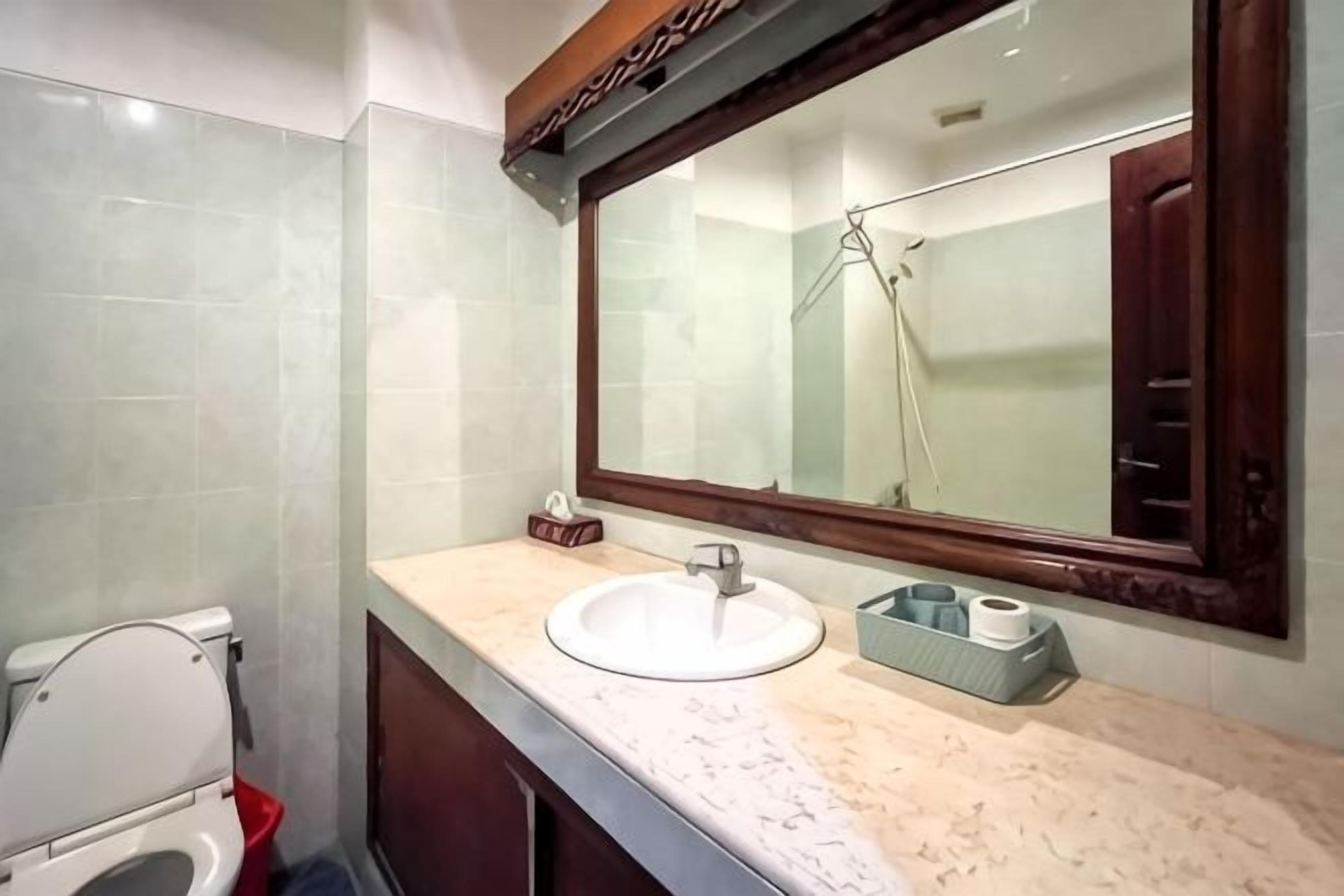 A bathroom with a white toilet, a sink with a marble countertop, and a large mirror above the sink.